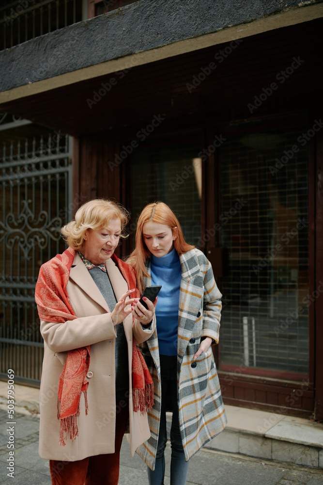 A grandmother and her grandchild standing on the street and reading messages on the phone. A grandmother and her grandchild standing on the street and reading messages on the phone.