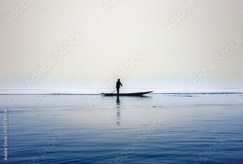 Silhouette of a person in a boat(shikara) rowing in partial frozen dal lake in Kashmir, Srinagar. 