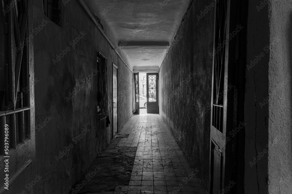 Photo inside the corridor of an old apartment building, the sun shines through the windows and front door