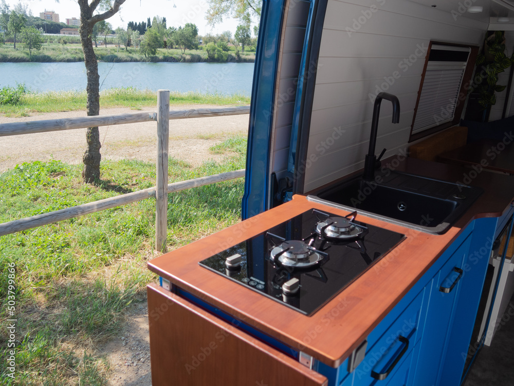 Interior de una camperizada, con cocina azul, grifo