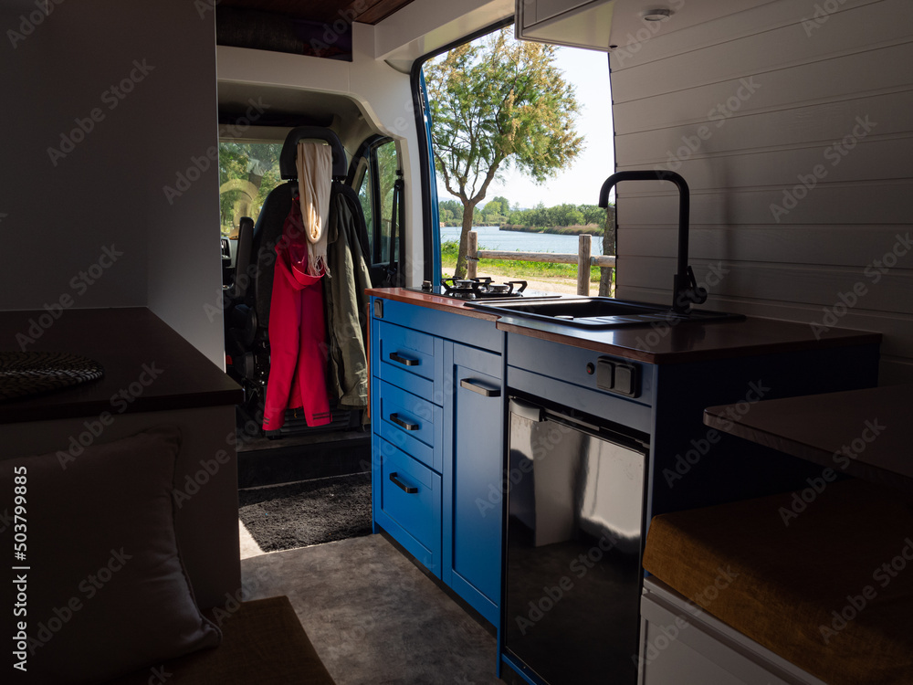 Interior de una camperizada, con cocina azul, grifo