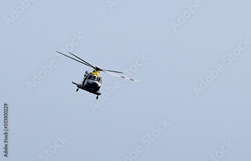 Yellow and white approaching helicopter frontal view, flying in the blue sky