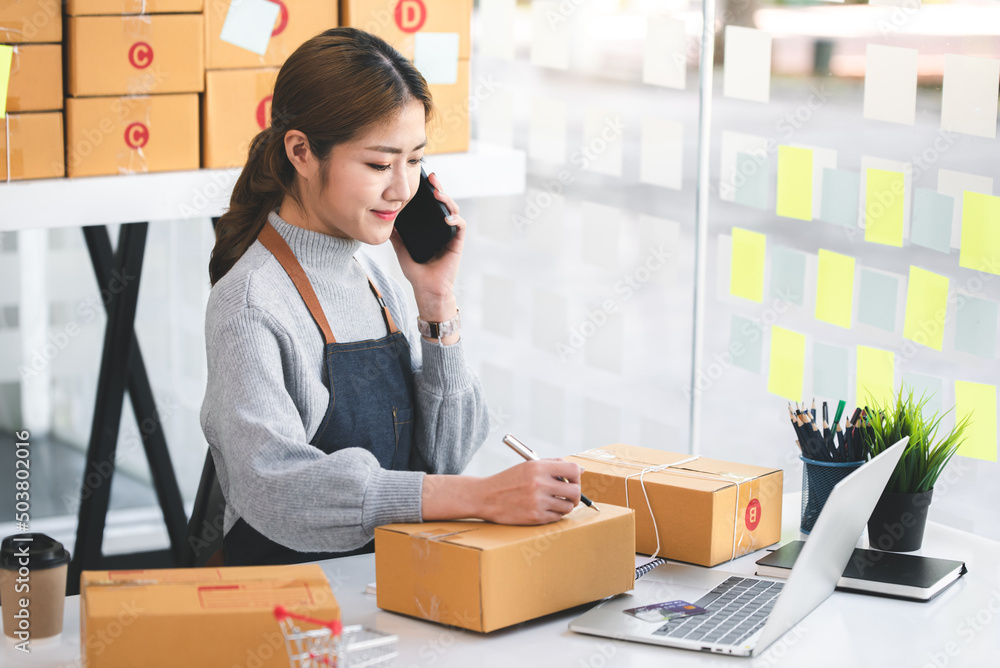 Portrait of a Small Business Startup, SME Owner, Female Entrepreneur work on parcel boxes Receipts and check orders online to prepare boxes. Selling to customers. Online SME business idea. Portrait of a Small Business Startup, SME Owner, Female Entrepreneur work on parcel boxes Receipts and check orders online to prepare boxes. Selling to customers. Online SME business idea.