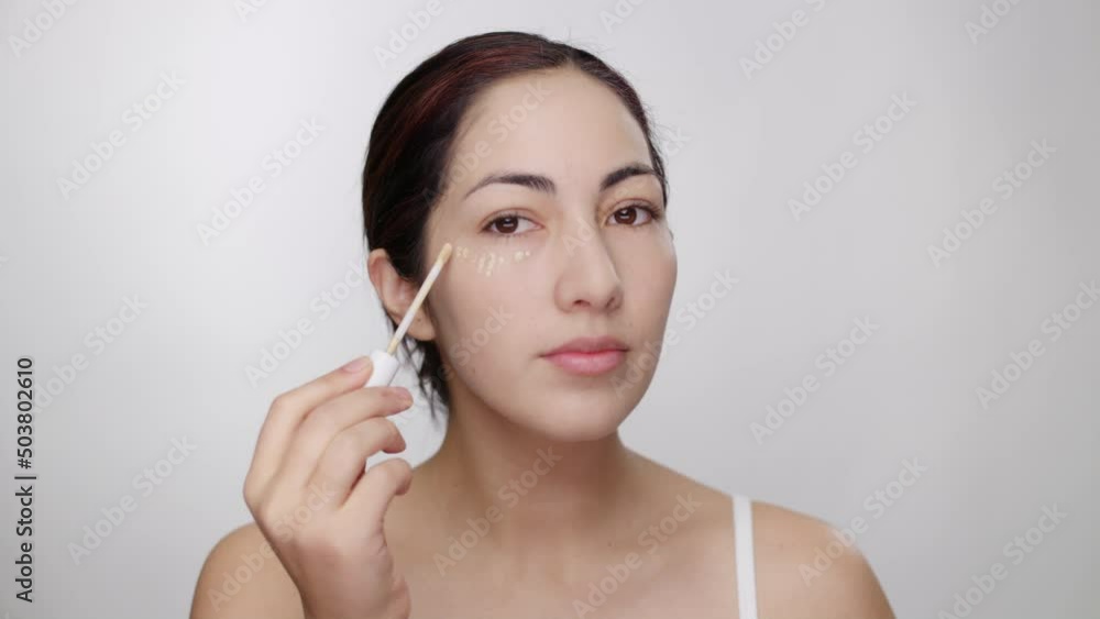 Female model demonstrates application of concealer under eye, blends with brush Female model demonstrates application of concealer under eye, blends with brush