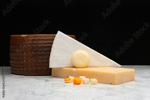 Closeup image of a akawi and Cheddar cheese and a small round cheese with a brown basket photo