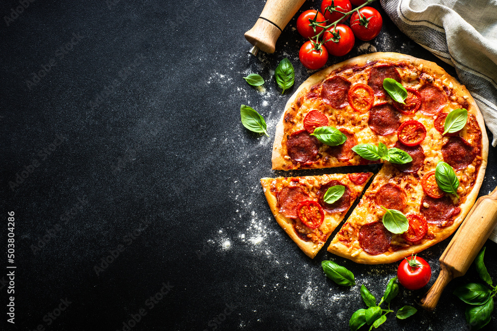 Pizza on black background. Traditional italian pizza with salami cheese, tomatoes and basil. Top view with copy space.