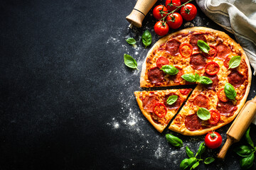 Pizza on black background. Traditional italian pizza with salami cheese, tomatoes and basil. Top view with copy space.