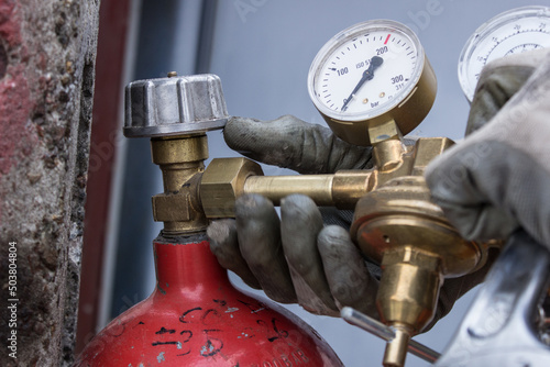 Red bottle for storing liquefied gas. Gas cylinder. Close-up plan of Men's hands in gloves screwing the reducer on the gas cylinder. Concept for content about fuel, gas or welding.