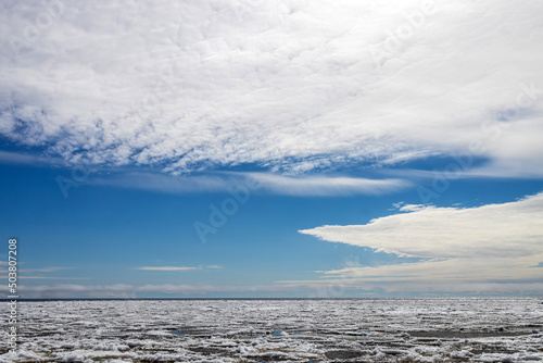 Lake Ladoga covered with ice in front of the icebreaker. The sky with light cirrus clouds is reflected in the water
