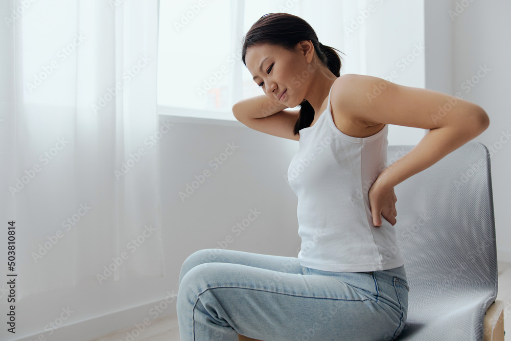Back pain. Suffering from osteochondrosis after long study work pretty young Asian woman touching painful lower back at home interior living room. Injuries Poor health Illness concept. Cool offer Back pain. Suffering from osteochondrosis after long study work pretty young Asian woman touching painful lower back at home interior living room. Injuries Poor health Illness concept. Cool offer