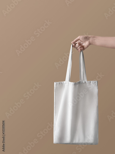 Eco bag. Concept photo with copy space. Girl is holding white canvas bag in her hand against beige backdrop