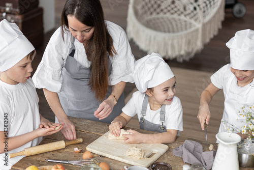 Mother and her little cute kids baking homemade sweet pie together  having fun. Home bakery  little kids in process of food preparation in the kitchen at home  helping mother  doing chores