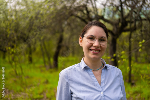 Portrait of a young beautiful brunette woman with glasses in a blooming garden in summer afternoon on a sunny day. Suburban rural life