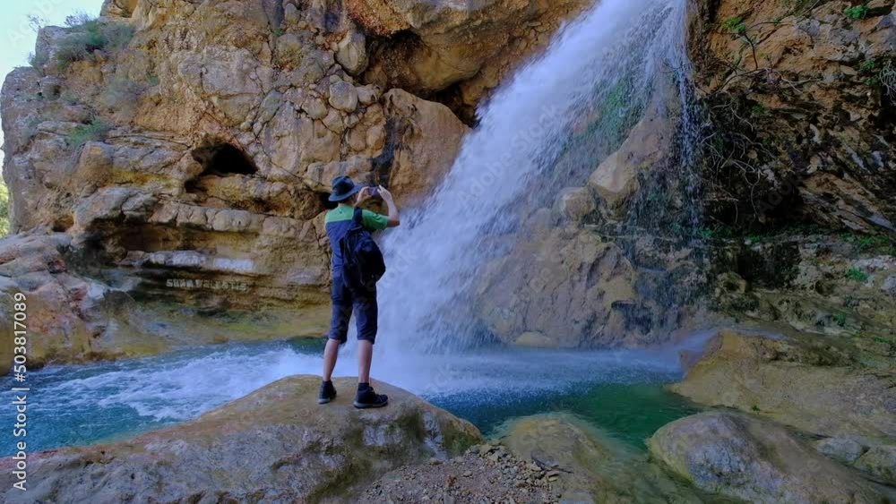 Man is holding a mobile phone and taking a photo of a beautiful waterfall. Hiking in nature. Slow motion video. Man is holding a mobile phone and taking a photo of a beautiful waterfall. Hiking in nature. Slow motion video.
