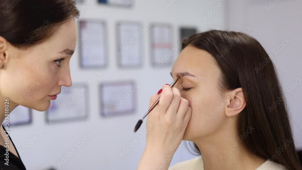process of eyebrow coloring procedure in beauty salon. woman professional stylist dyeing female client's brows with brown tint, using make-up brush, henna paint. cosmetology, beautician occupation process of eyebrow coloring procedure in beauty salon. woman professional stylist dyeing female client's brows with brown tint, using make-up brush, henna paint. cosmetology, beautician occupation