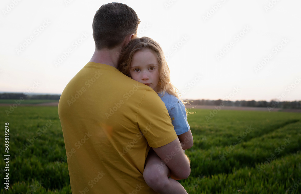 father carrying a tired daughter through a field at sunset father carrying a tired daughter through a field at sunset