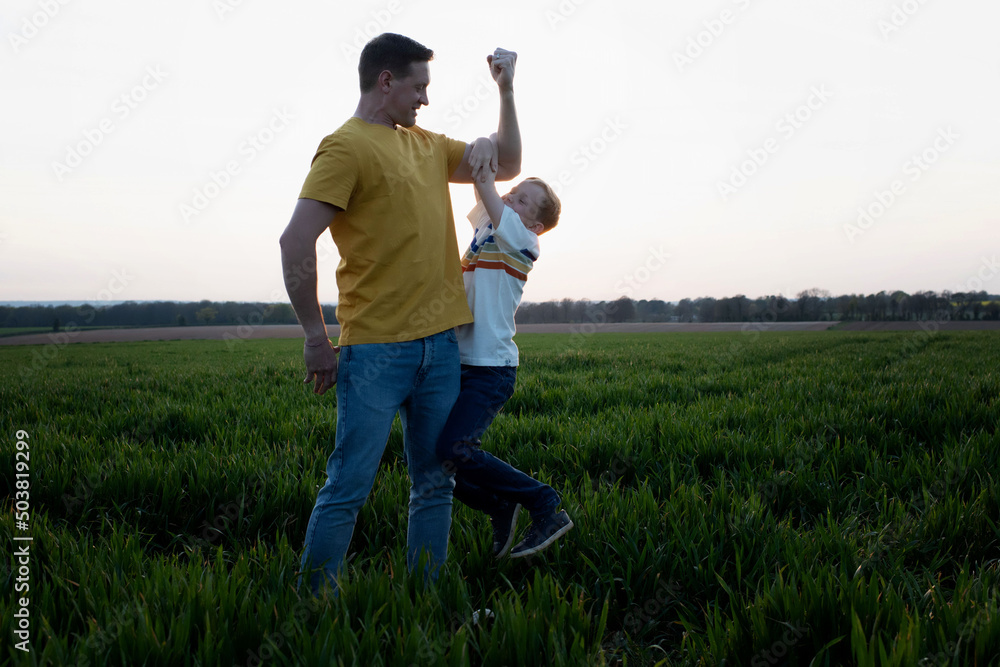 father flexing his muscles whilst son hangs on his arm playfully father flexing his muscles whilst son hangs on his arm playfully
