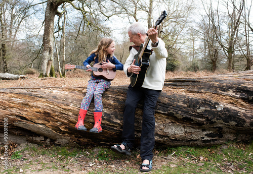 grandfather teaching his granddaughter to play guitar in the forest