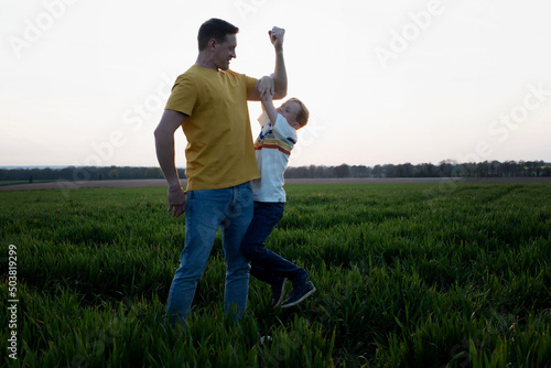 father flexing his muscles whilst son hangs on his arm playfully photo