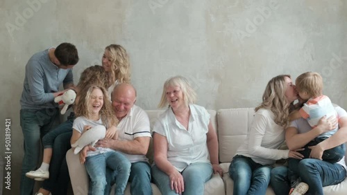 Portrait of large Caucasian family of three generations sitting on sofa in living room house. Happy big family together for weekend. Children run up to their adult parents and hug them