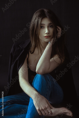 Young brunette in blue jeans and jacket on a black background photo