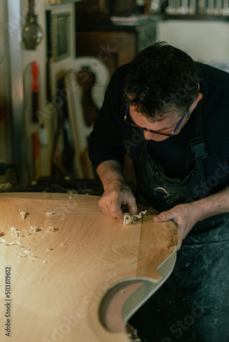 luthier carving creating wood chips on a double bass front table photo