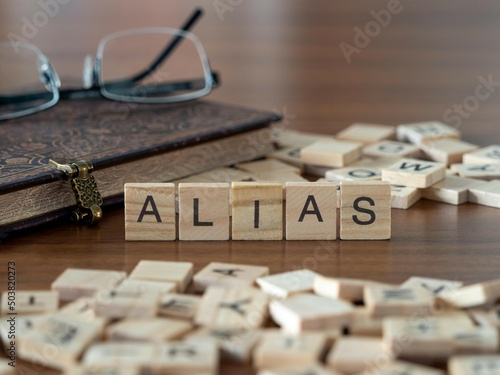 alias word or concept represented by wooden letter tiles on a wooden table with glasses and a book photo