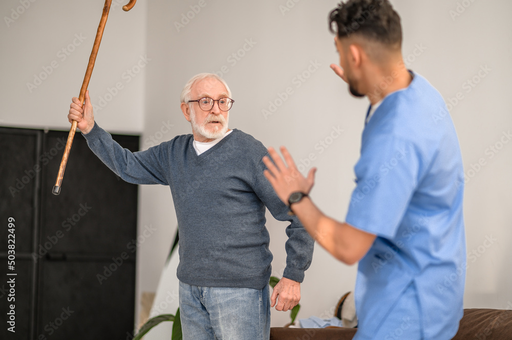 Exasperated pensioner threatening his caretaker with his cane Exasperated pensioner threatening his caretaker with his cane