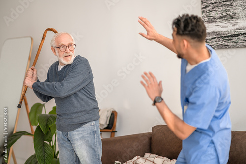 Canvastavla Aggressive pensioner brandishing the walking stick at his caretaker