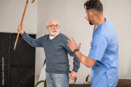 Exasperated pensioner threatening his caretaker with his cane Fototapet