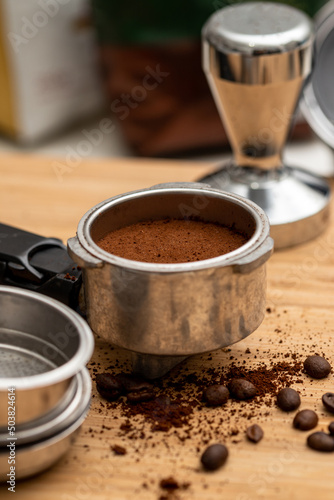 Ground and compressed coffee in the filter holder with coffee beans scattered around