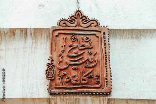 Metallic board with Arabic hieroglyphs on a textured wall with stains photo