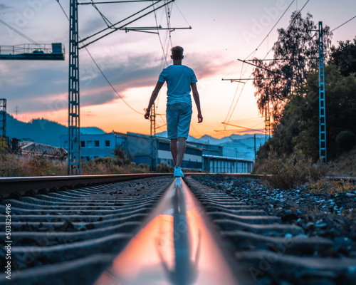 Back view of a young Caucasian man walking on the railroad at sunset in Slovakie photo