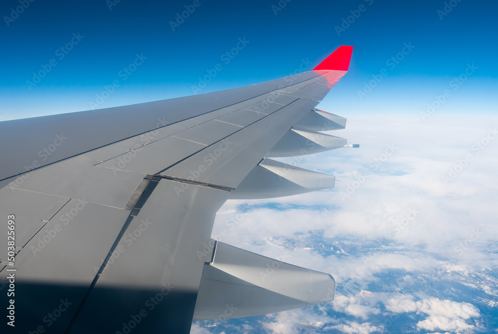 Fototapeta premium View from passenger cabin window on wing of flying plane against background of blue sky and white clouds