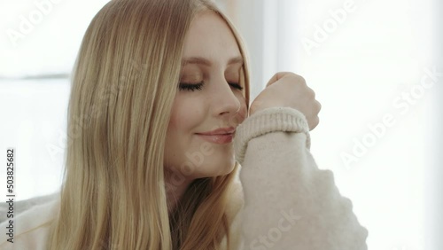 Blonde woman smells essential oil perfume on wrist while sitting on couch