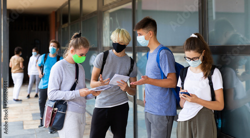 Group of students in protective masks discuss past lessons at a college on the street