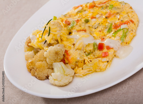 Vegetable omelet with garnish of baked cauliflower sprinkled with grated cheese on white plate..