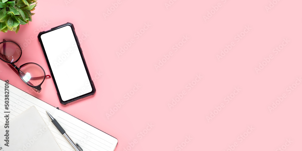 Office desk with Blank screen smart phone, Pen, Notebook, eyeglass on pink background, Top view with copy space, Mock up.. Office desk with Blank screen smart phone, Pen, Notebook, eyeglass on pink background, Top view with copy space, Mock up..