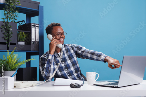 Marketing company happy joyful african american office worker on landline call with accountant talking about expenses report. Cheerful smiling manager on telephone conversation with team leader photo