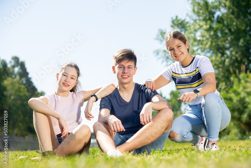 Group of teenagers chatting while sitting on green spring lawn