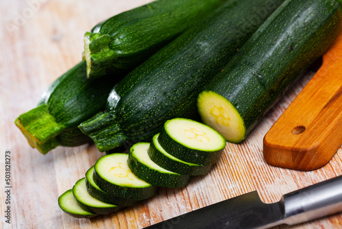 Whole and sliced fresh zucchini on wooden table. Healthy vegetarian ingredient