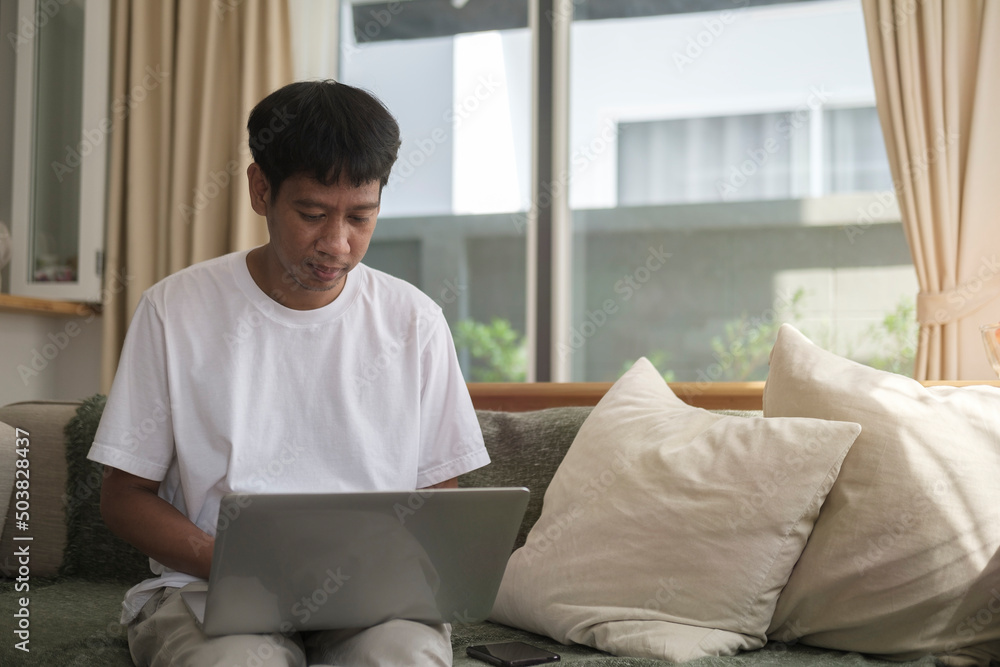 Smiling handsome asian man sitting on floor in living room and using laptop computer.. Smiling handsome asian man sitting on floor in living room and using laptop computer..
