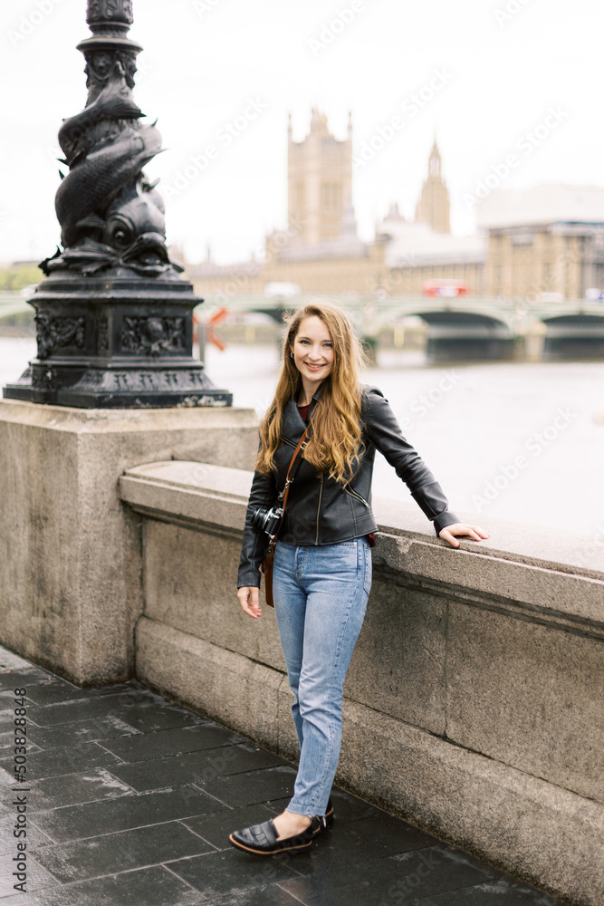 A young Caucasian woman in her 20s smiling in a fashionable black leather jacket in the city of London, UK.
