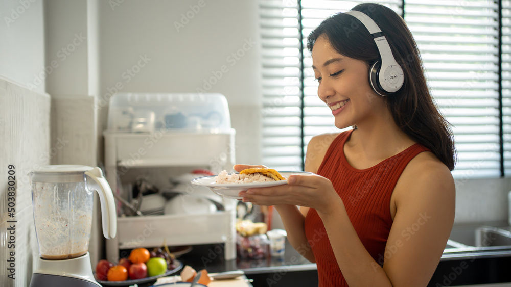 Beautiful young woman cooking in the kitchen at home while listening to music through headphones - lifestyles concepts Beautiful young woman cooking in the kitchen at home while listening to music through headphones - lifestyles concepts