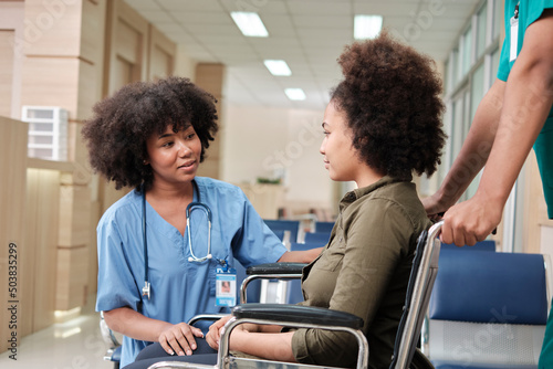 Young African American female doctor with stethoscope in uniform checks injury patient girl in wheelchair at outpatient accident clinic hospital, illness medical clinic examination, healthcare hall.