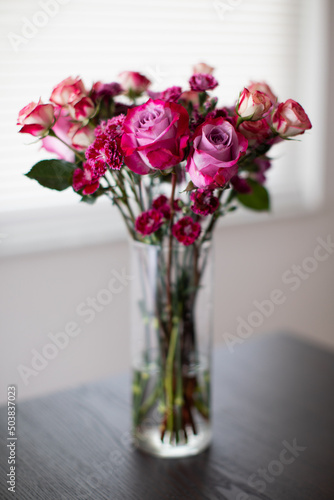 bouquet of roses  tulips  carnations in a clear vase on a wooden table in front of a window at the home