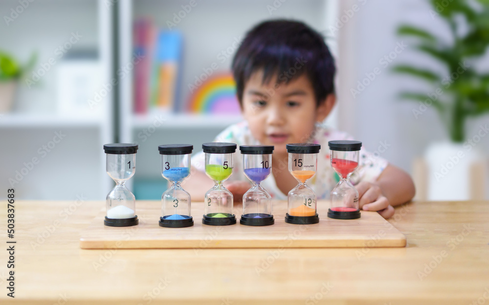 Blurred of 3 years old asian little boy is looking set of hourglass with difference time and observe the flow of colorful sand, concept of begin of time learning for kid, homeschool, activity for kid. Blurred of 3 years old asian little boy is looking set of hourglass with difference time and observe the flow of colorful sand, concept of begin of time learning for kid, homeschool, activity for kid.