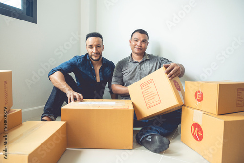 LGBTQ couples are packing boxes to move house. They lived happily ever after, covering the boxes with tape to prepare them for transport. © PIPAT