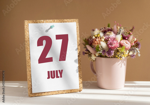 july 27. 27th day of month, calendar date.Bouquet of dead wood in pink mug on desktop.Cork board with calendar sheet on white-beige background. Concept of day of year, time planner, summer month