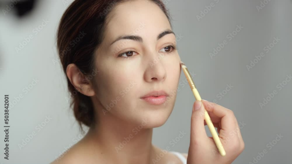 Makeup tutorial: Side view, lovely brunette woman applies foundation with brush Makeup tutorial: Side view, lovely brunette woman applies foundation with brush
